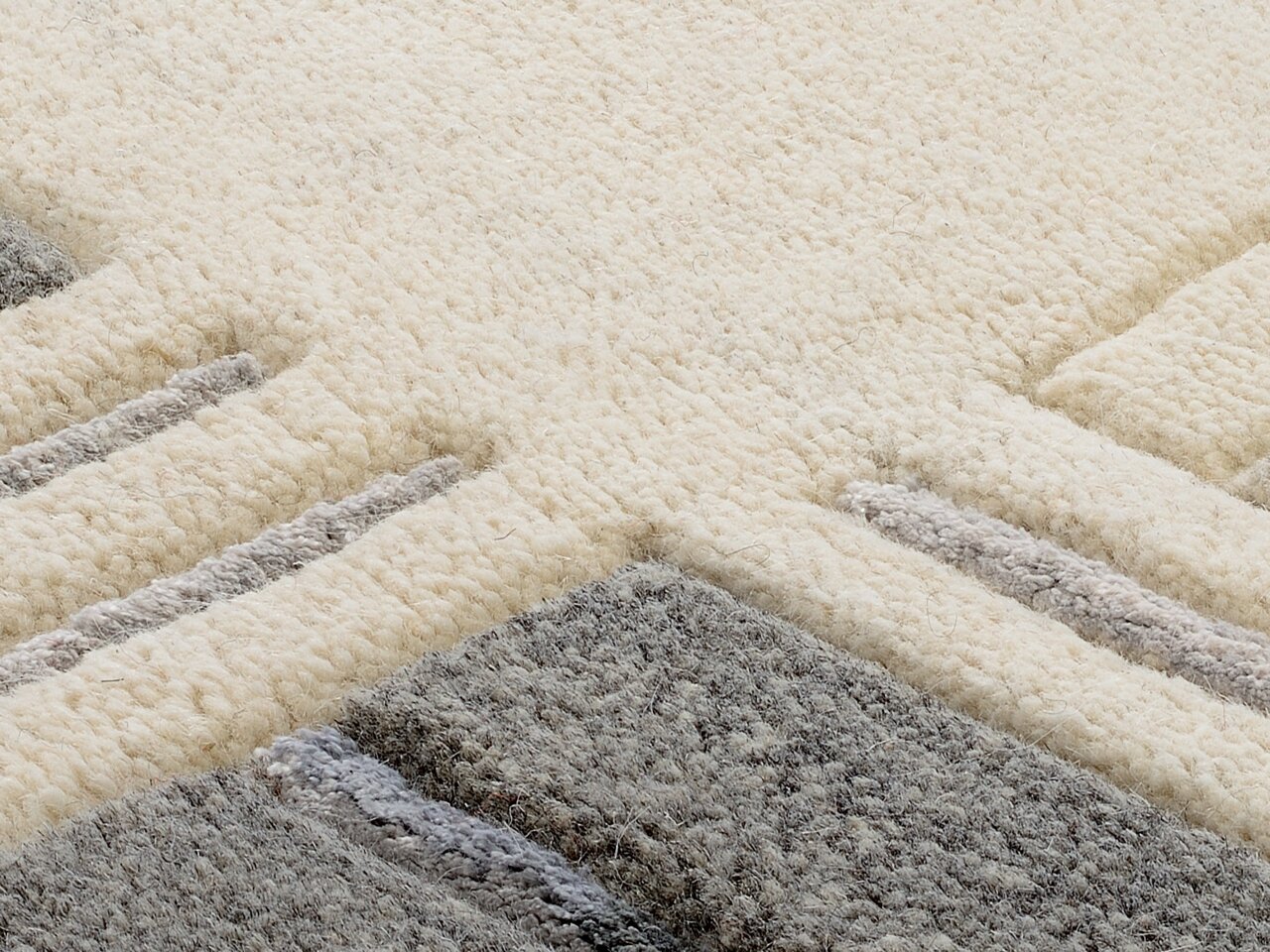 Nahaufnahme eines Wollteppichs mit geometrischem Muster in Creme- und Grautönen, aus seitlicher Perspektive fotografiert.