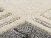 Nahaufnahme eines Wollteppichs mit geometrischem Muster in Creme- und Grautönen, aus seitlicher Perspektive fotografiert.