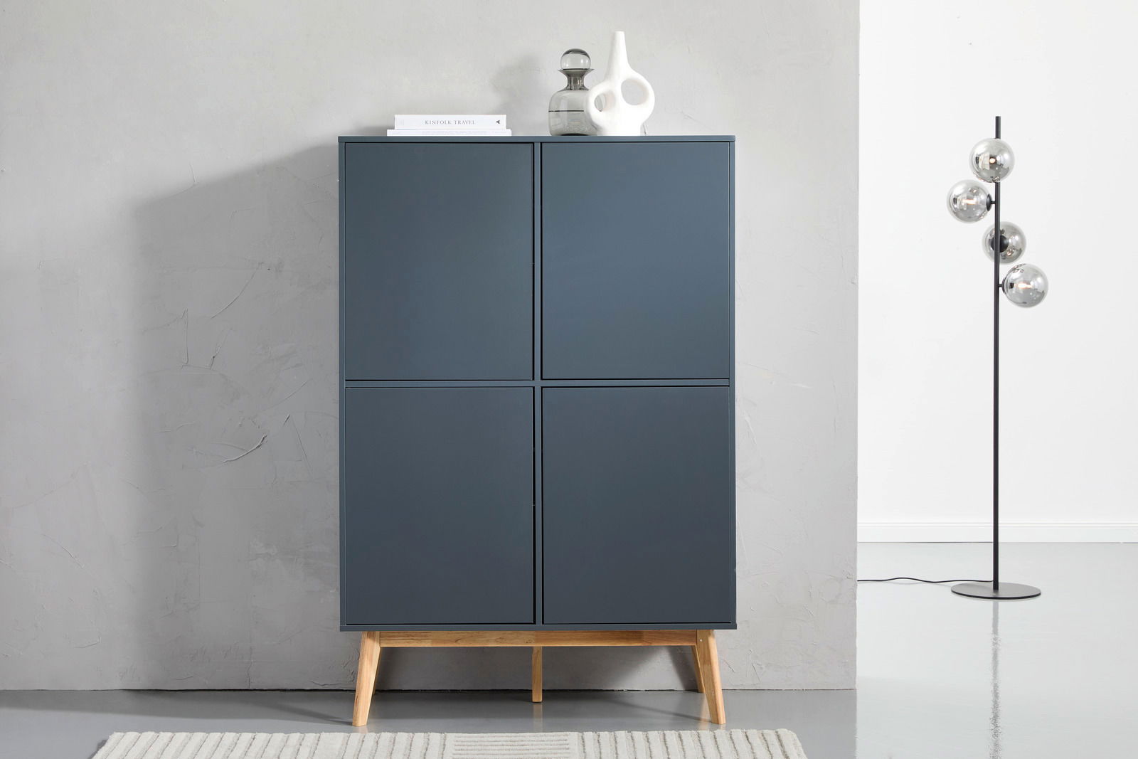 Modernes Highboard in dunklem Blau mit vier Türen, auf Holzbeinen stehend, frontal fotografiert.