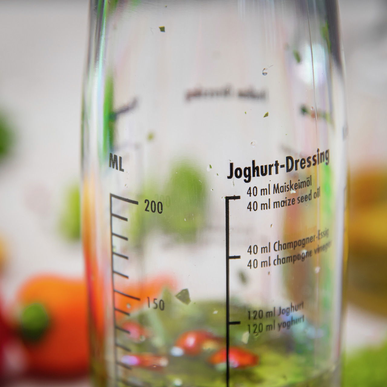 Nahaufnahme eines Dressing-Shakers mit Messskala und Rezept für Joghurt-Dressing auf der Glasoberfläche.