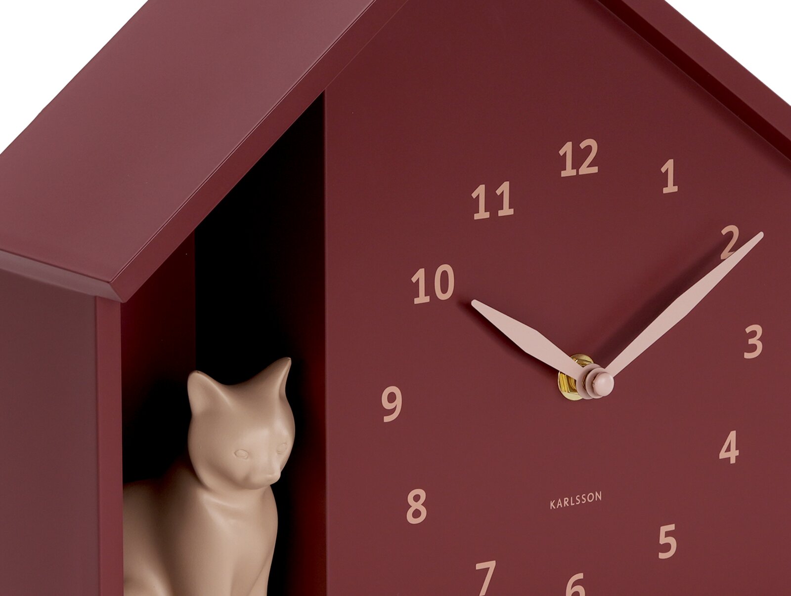 Nahaufnahme einer burgunderroten Wanduhr in Hausform mit einer kleinen Katzenfigur im Inneren. Die Uhr hat beige Zeiger und Ziffern. Perspektive von vorne leicht seitlich.