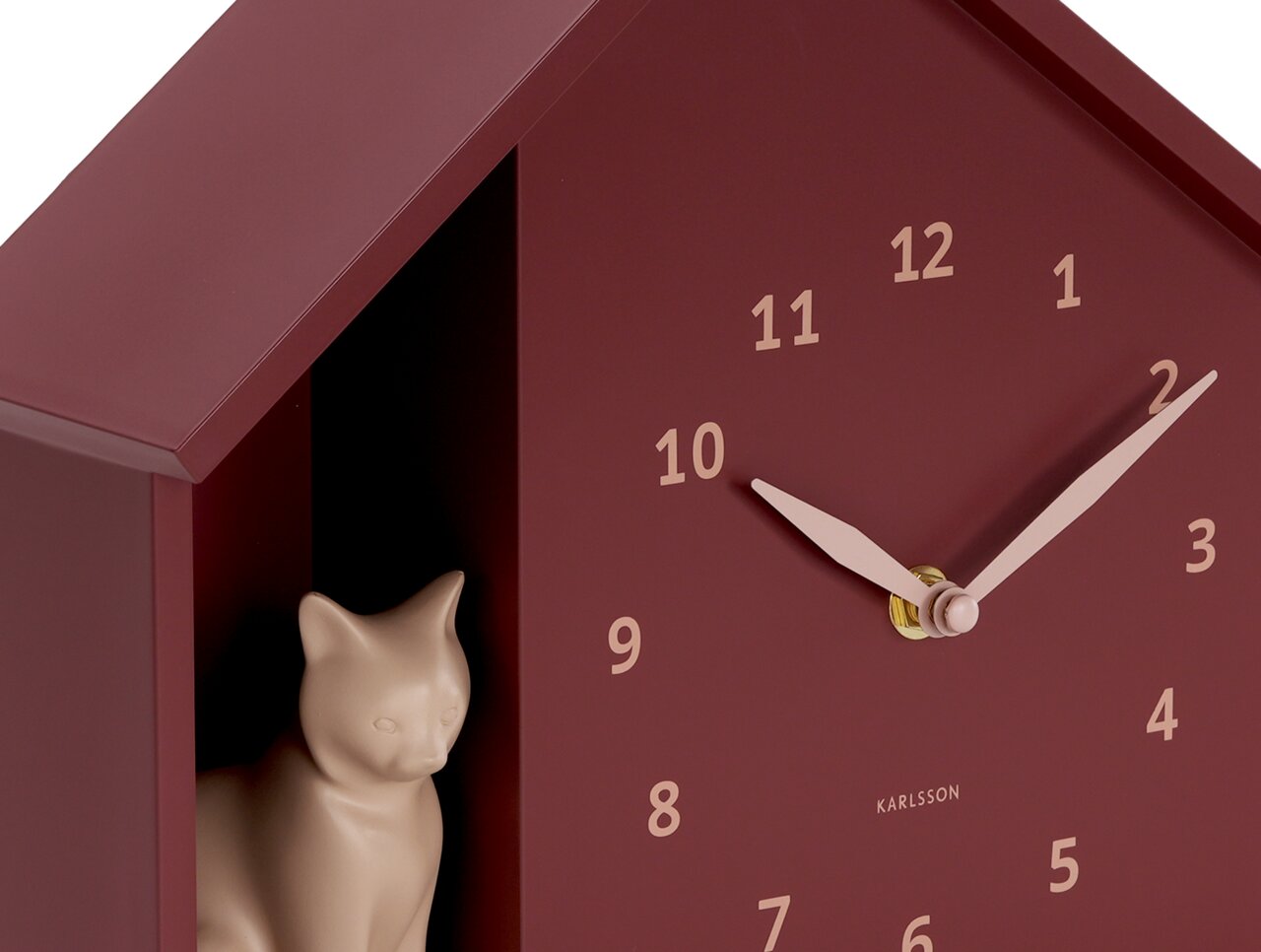 Nahaufnahme einer burgunderroten Wanduhr in Hausform mit einer kleinen Katzenfigur im Inneren. Die Uhr hat beige Zeiger und Ziffern. Perspektive von vorne leicht seitlich.