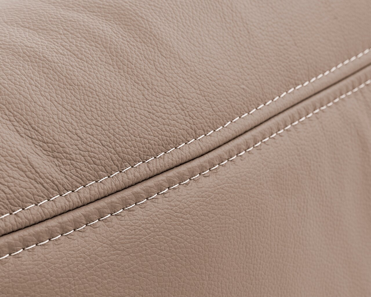 Nahaufnahme einer beigen, strukturierten Lederoberfläche mit sichtbaren Nähten, perspektivisch von der Seite aufgenommen.
