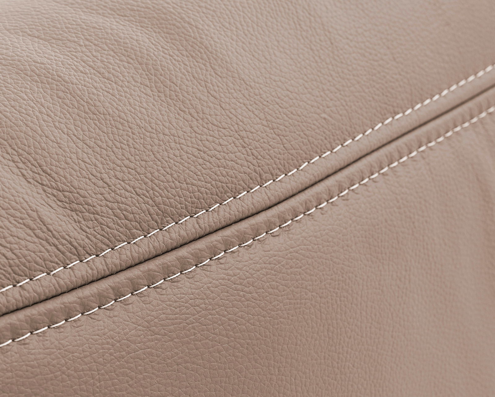 Nahaufnahme einer beigen, strukturierten Lederoberfläche mit sichtbaren Nähten, perspektivisch von der Seite aufgenommen.