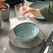 Türkise Müslischale Lave 380ml auf einem passenden Teller, von oben betrachtet, neben einem Glas in einer Hand.