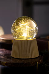 Leuchtende Schneekugel mit Sternmotiv auf einem Tisch, seitliche Perspektive