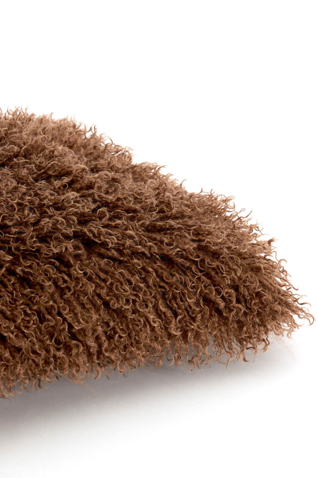 Nahaufnahme eines braunen, flauschigen Kissens mit lockiger Textur, seitliche Perspektive
