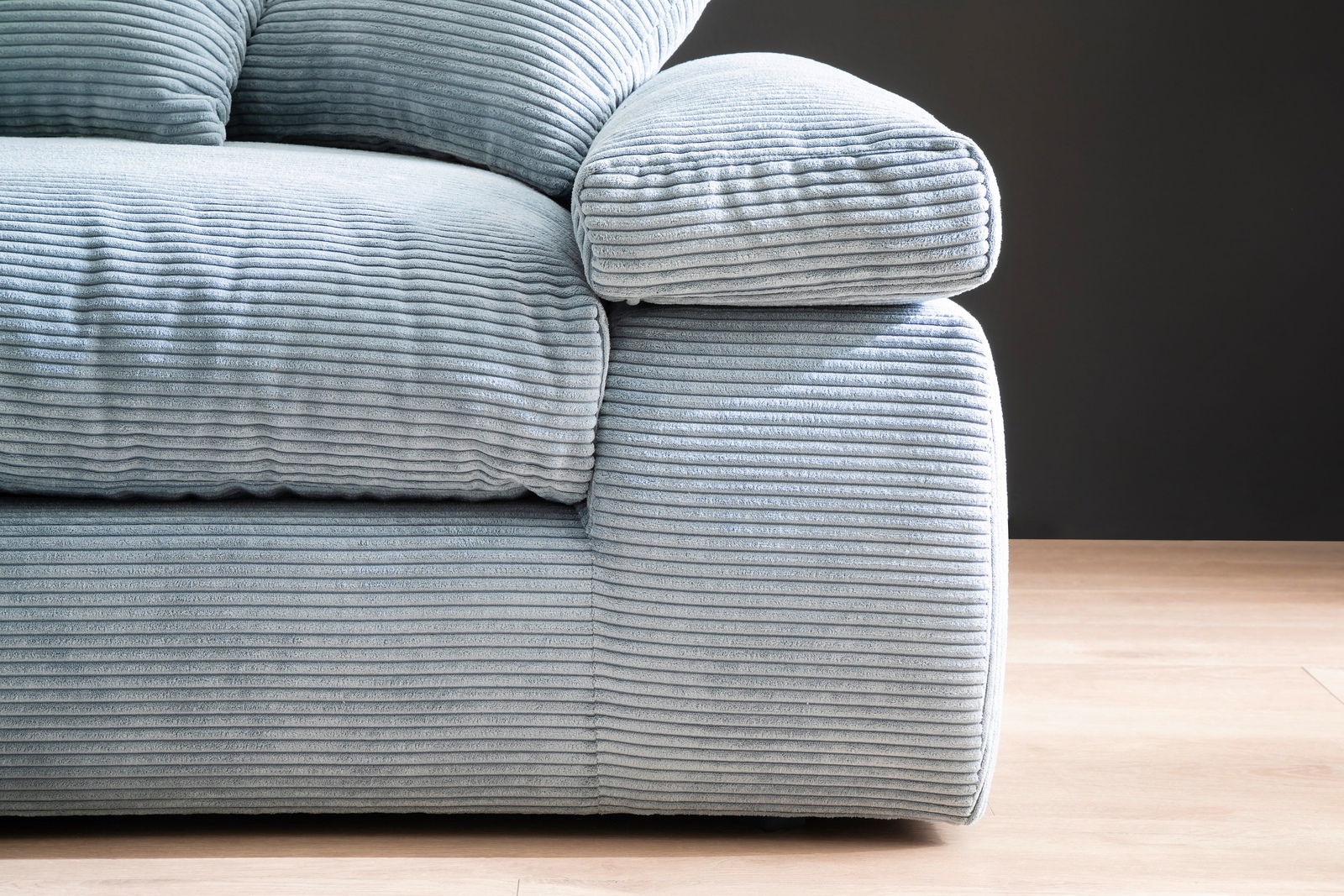 Nahaufnahme eines Big-Sofas mit geripptem Stoffbezug in hellblau, seitliche Perspektive.