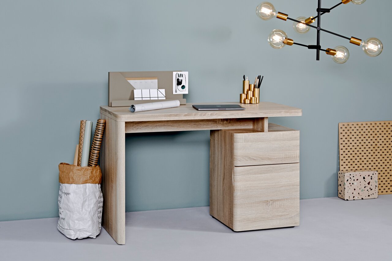 Moderner Schreibtisch aus hellem Holz mit Schubladen, seitlicher Perspektive, dekoriert mit Schreibutensilien und Laptop.