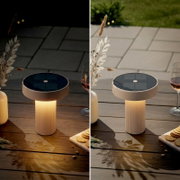 Solarbetriebene LED-Tischleuchte für den Außenbereich mit rundem Solarpanel oben und geriffeltem Standfuß auf Holztisch, gezeigt in Seitenansicht leicht von oben (Tag- und Nachtstimmung).
