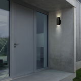 Moderne schwarze Akku-Außenwandleuchte an einer Betonwand neben einer Haustür, seitliche Perspektive.