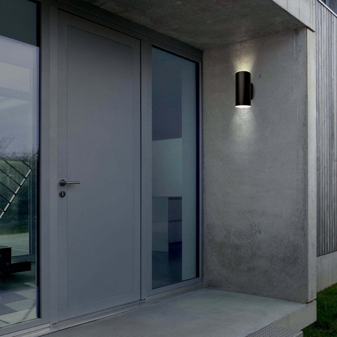 Moderne schwarze Akku-Außenwandleuchte an einer Betonwand neben einer Haustür, seitliche Perspektive.