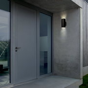 Moderne schwarze Akku-Außenwandleuchte an einer Betonwand neben einer Haustür, seitliche Perspektive.