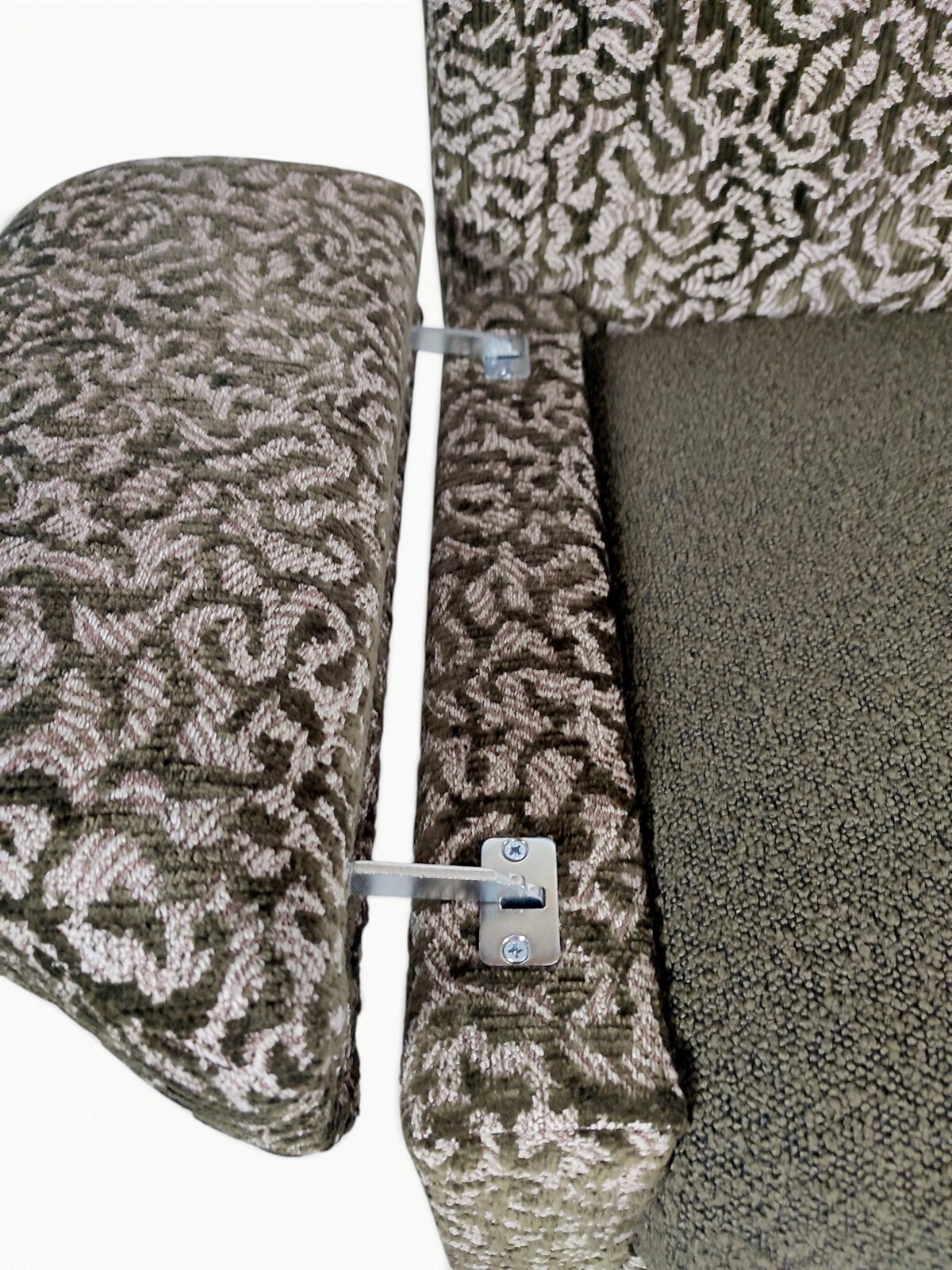 Detailansicht von oben: gepolsterte Sofalehne mit gemustertem Stoffbezug und sichtbaren Metall-Verbinderbeschlägen neben der Sitzfläche