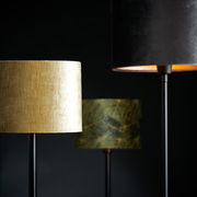 Drei Lampenschirme in verschiedenen Farben und Mustern, im Vordergrund ein goldener Zylinder-Lampenschirm, seitliche Perspektive.