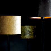 Drei Lampenschirme in verschiedenen Farben und Mustern, im Vordergrund ein goldener Zylinder-Lampenschirm, seitliche Perspektive.