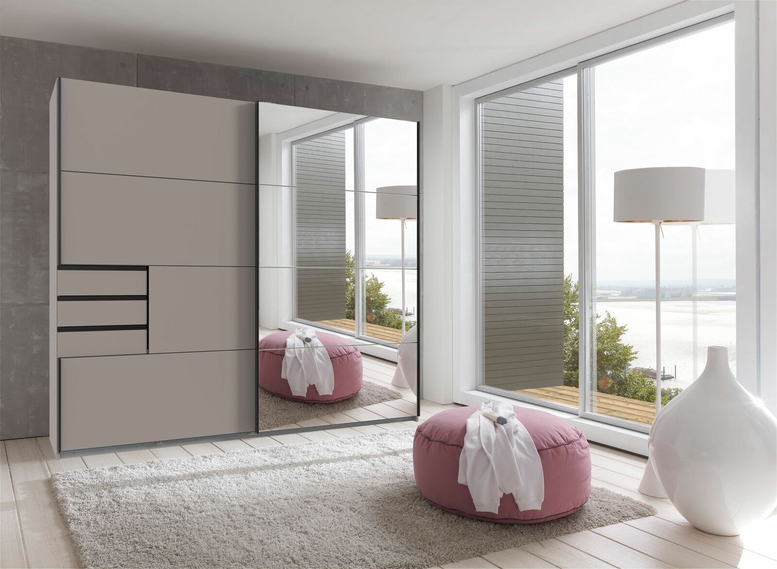 Moderner Schwebetürenschrank mit Spiegel in einem hellen Raum mit Blick auf das Wasser, von vorne betrachtet.