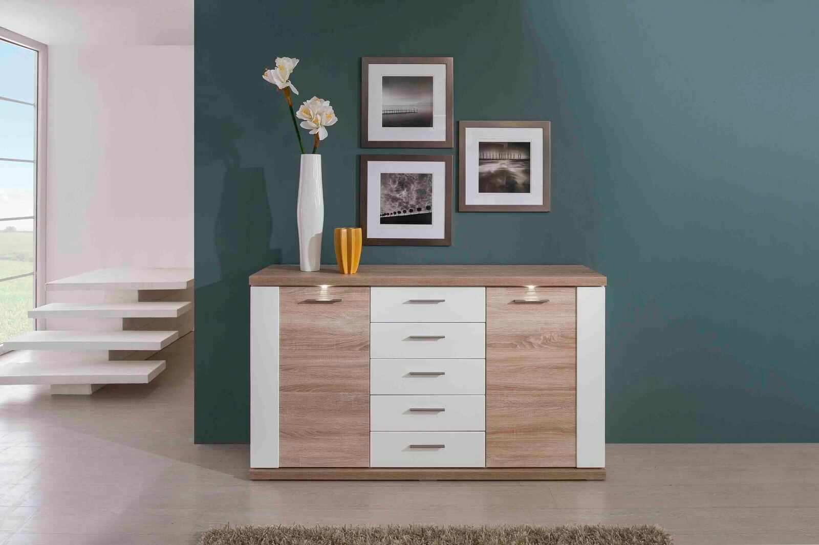 Frontale Ansicht eines modernen Sideboards mit Holz- und Weißelementen, dekoriert mit einer Vase und Bildern an der Wand.