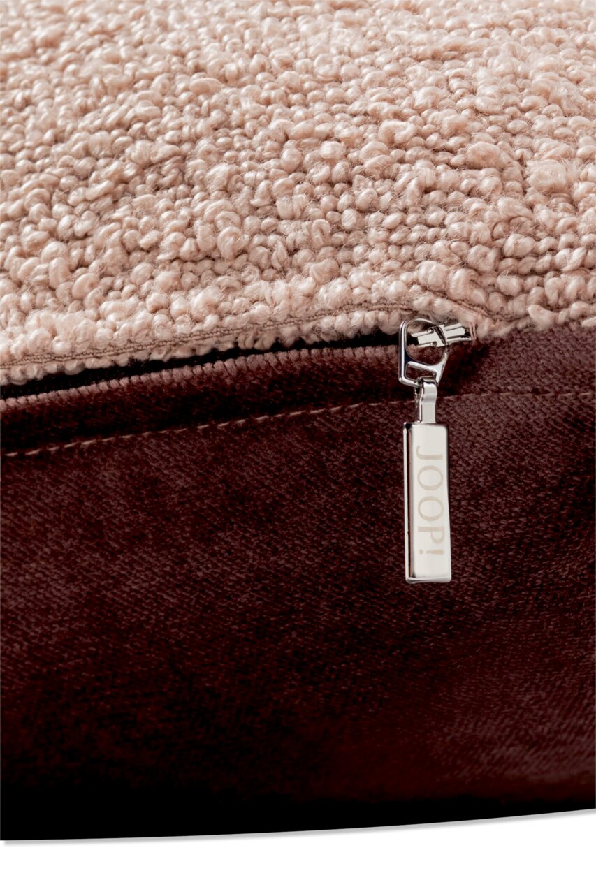 Nahaufnahme einer Zierkissenhülle mit weicher, strukturierter Oberfläche in Beige und einem braunen Reißverschluss mit JOOP!-Logo.