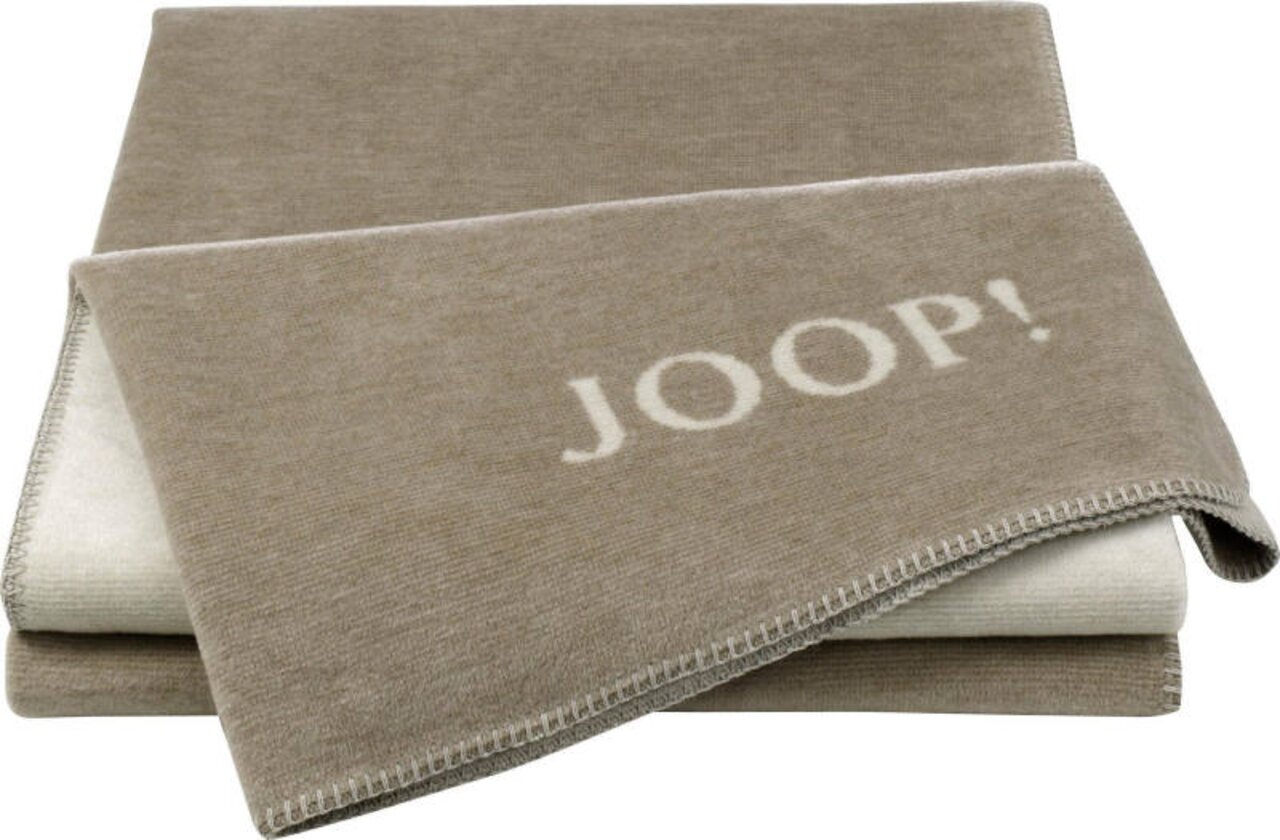 Beige Decke mit dem Schriftzug 'JOOP!' in Nahaufnahme, gefaltet auf einer weißen Oberfläche.