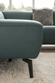 Nahaufnahme eines modernen Ecksofas in grünem Leder mit schwarzen Metallfüßen, seitliche Perspektive