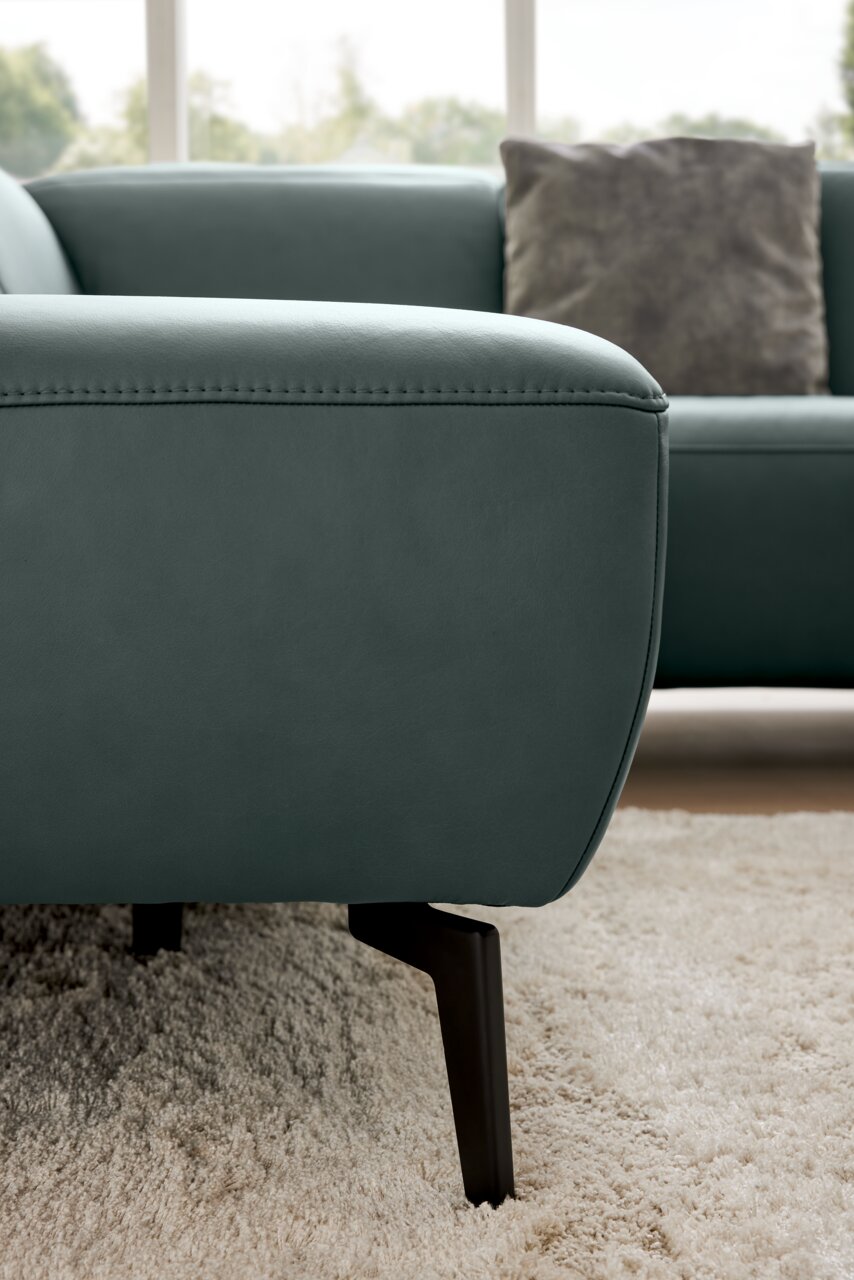 Nahaufnahme eines modernen Ecksofas in grünem Leder mit schwarzen Metallfüßen, seitliche Perspektive