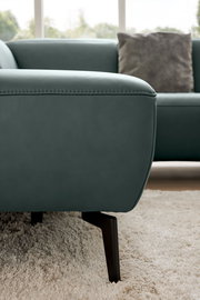 Nahaufnahme eines modernen Ecksofas in grünem Leder mit schwarzen Metallfüßen, seitliche Perspektive
