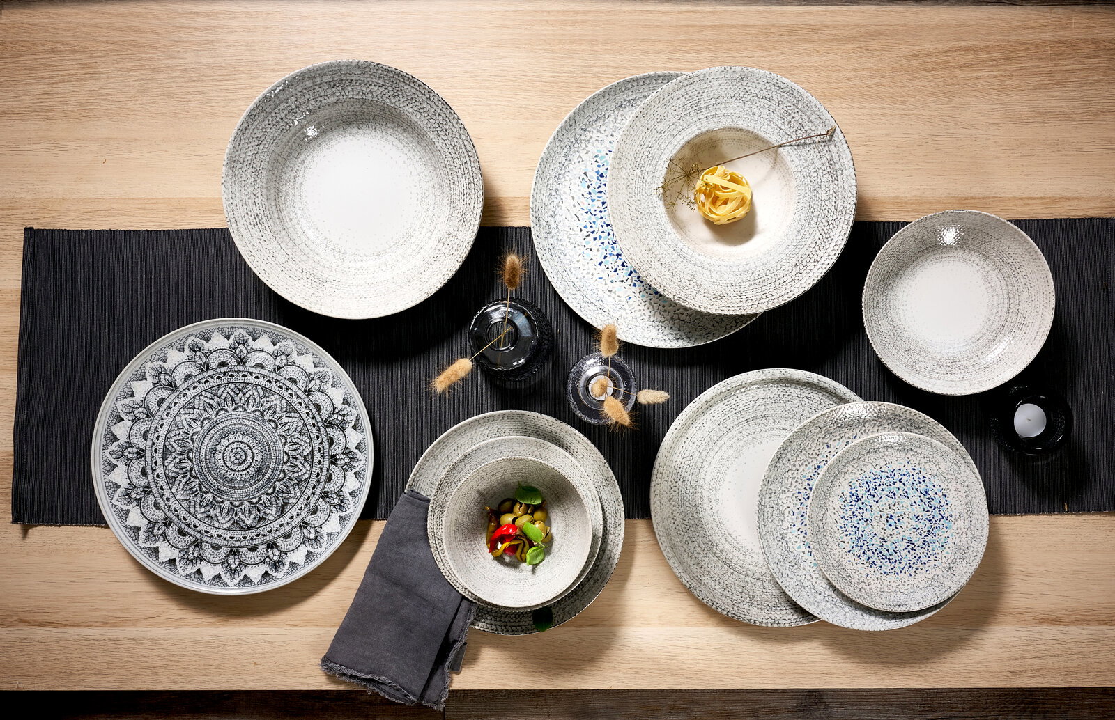 Verschiedene dekorative Platzteller und Schalen in einer Draufsicht auf einem Tisch arrangiert, mit einem kunstvollen Muster und natürlichen Farben.