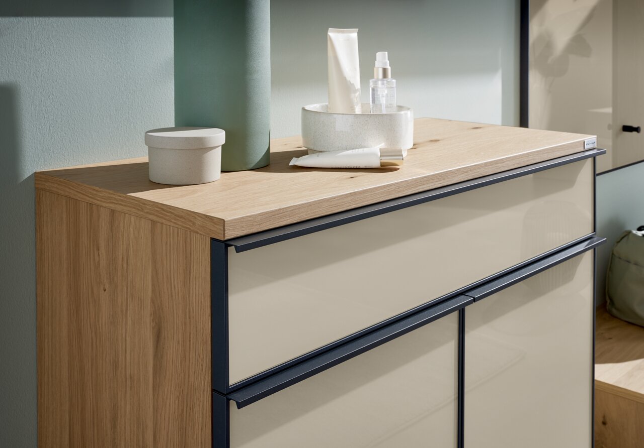 Close-up van een moderne schoenenkast met houten afwerking en crèmekleurige fronten, versierd met verzorgingsproducten en accessoires.