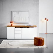 Frontale Ansicht eines modernen XL-Sideboards in Weiß mit Holzplatte, dekoriert mit einer orangefarbenen Lampe und Kunstwerk an der Wand.