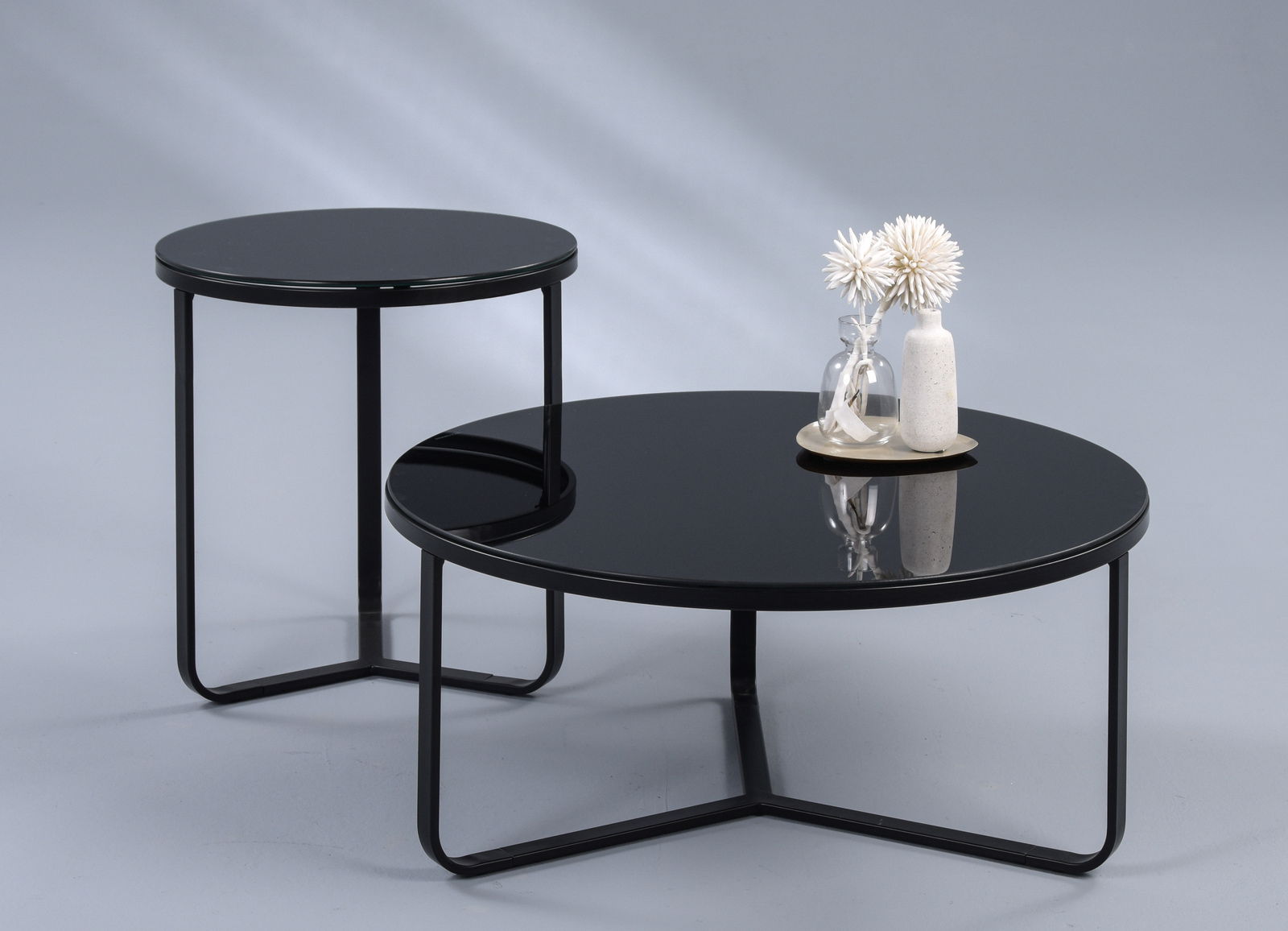 Zwei moderne Tische mit schwarzer Glasplatte und Metallgestell, einer als Beistelltisch und der andere als Couchtisch, aus seitlicher Perspektive fotografiert.