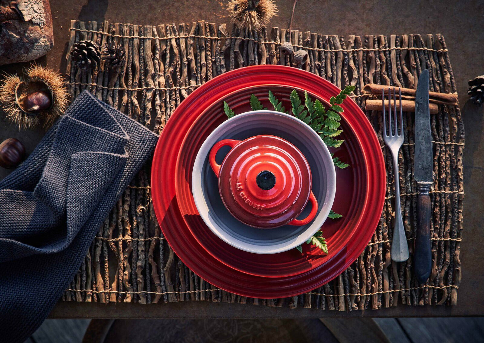 Obenansicht einer roten LE CREUSET Mini-Cocotte auf einem gedeckten Tisch mit rustikaler Dekoration.