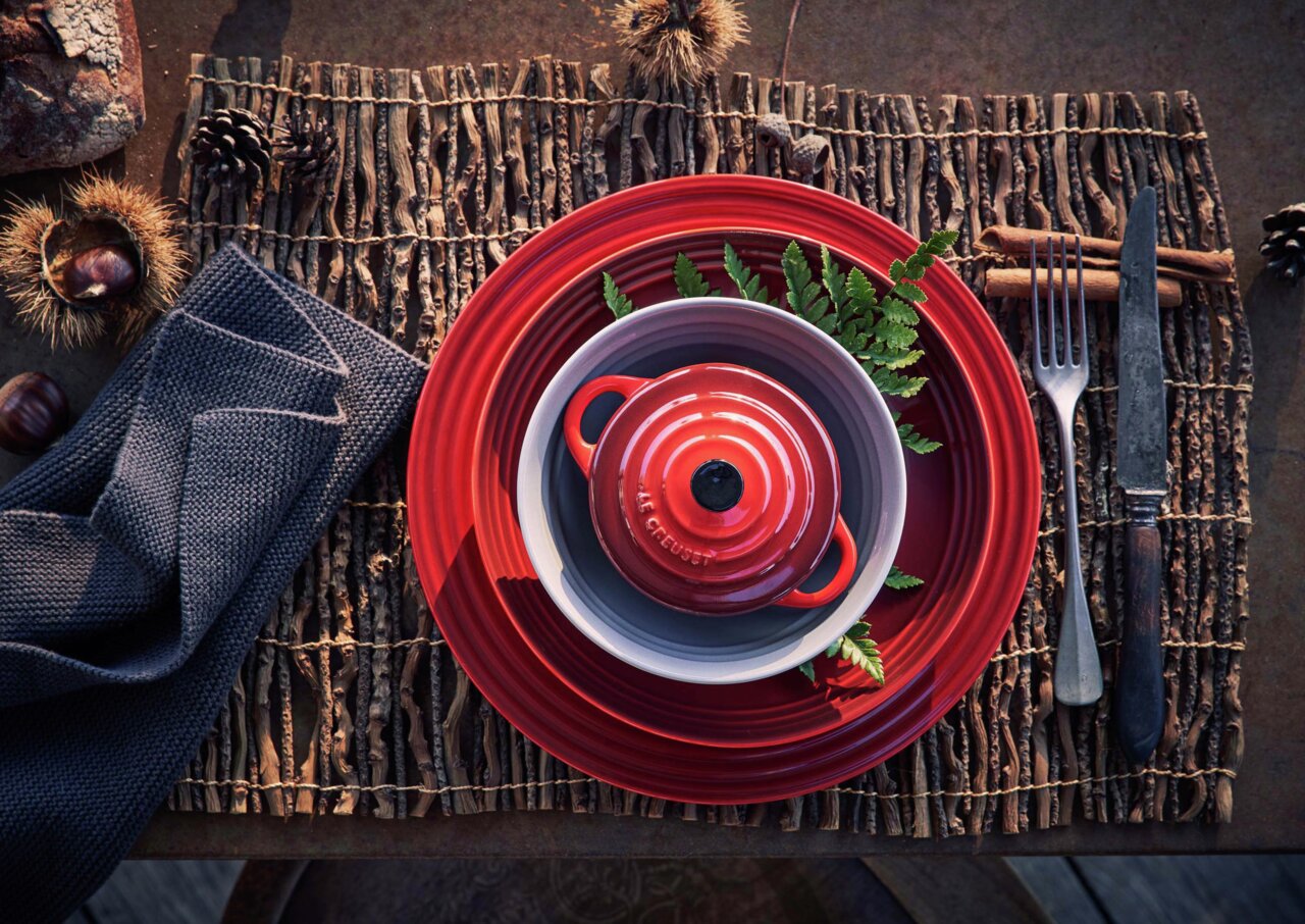 Obenansicht einer roten LE CREUSET Mini-Cocotte auf einem gedeckten Tisch mit rustikaler Dekoration.