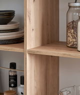 Nahaufnahme eines Holzregals mit Geschirr und Vorratsgläsern, seitliche Perspektive.