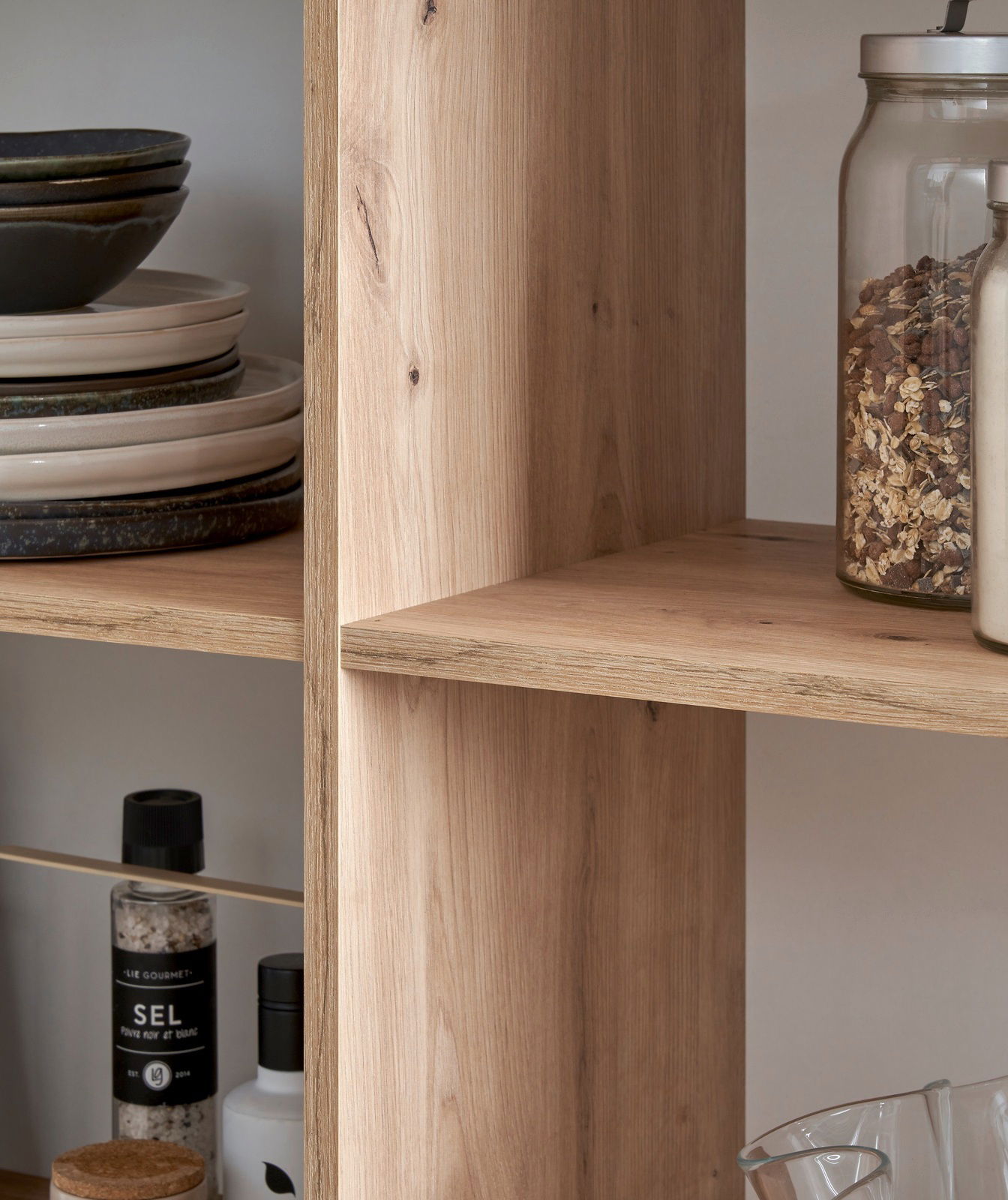 Nahaufnahme eines Holzregals mit Geschirr und Vorratsgläsern, seitliche Perspektive.