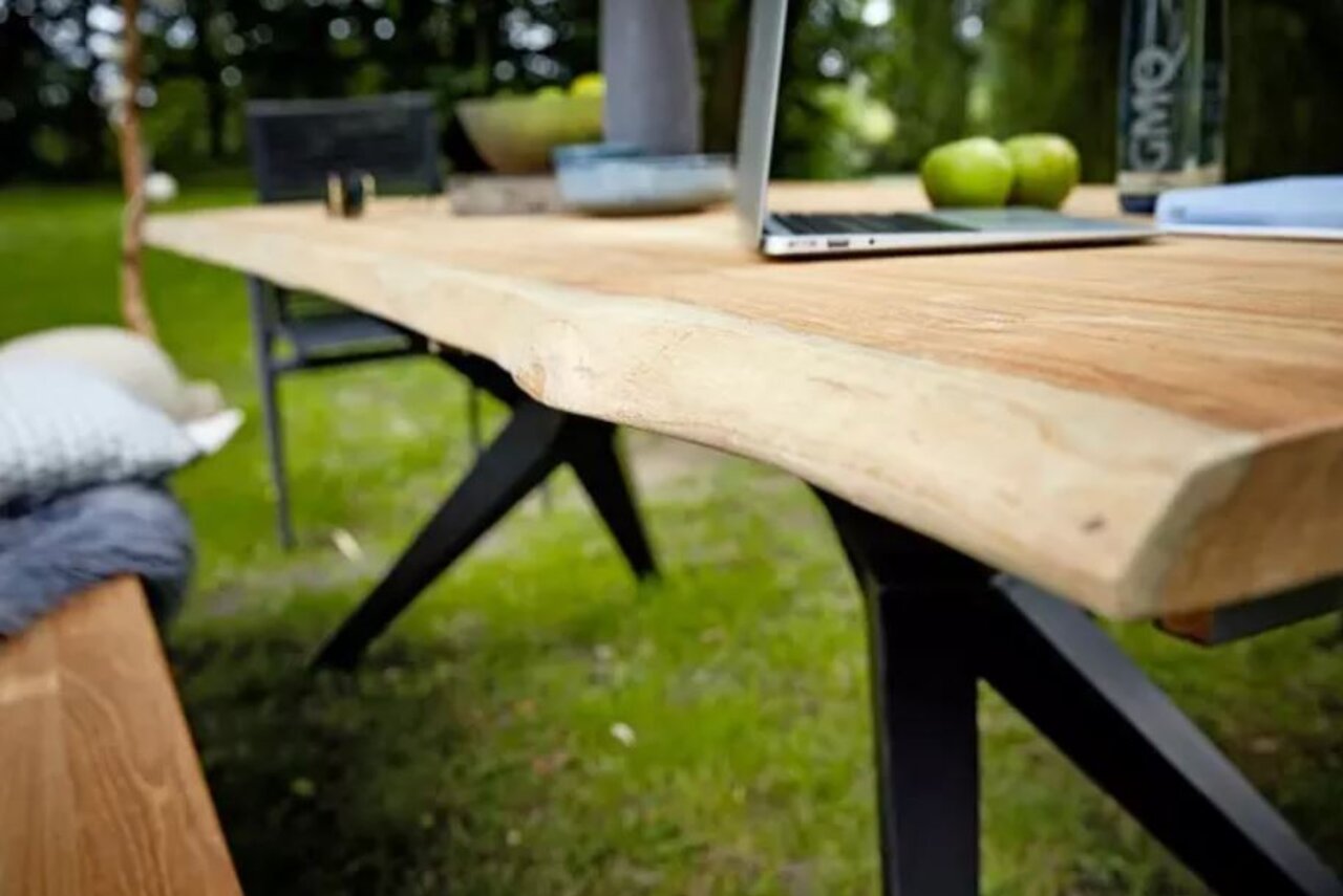 Nahaufnahme eines Esstisches aus Holz mit natürlicher Kante, im Freien aufgestellt, mit Laptop und Äpfeln darauf.