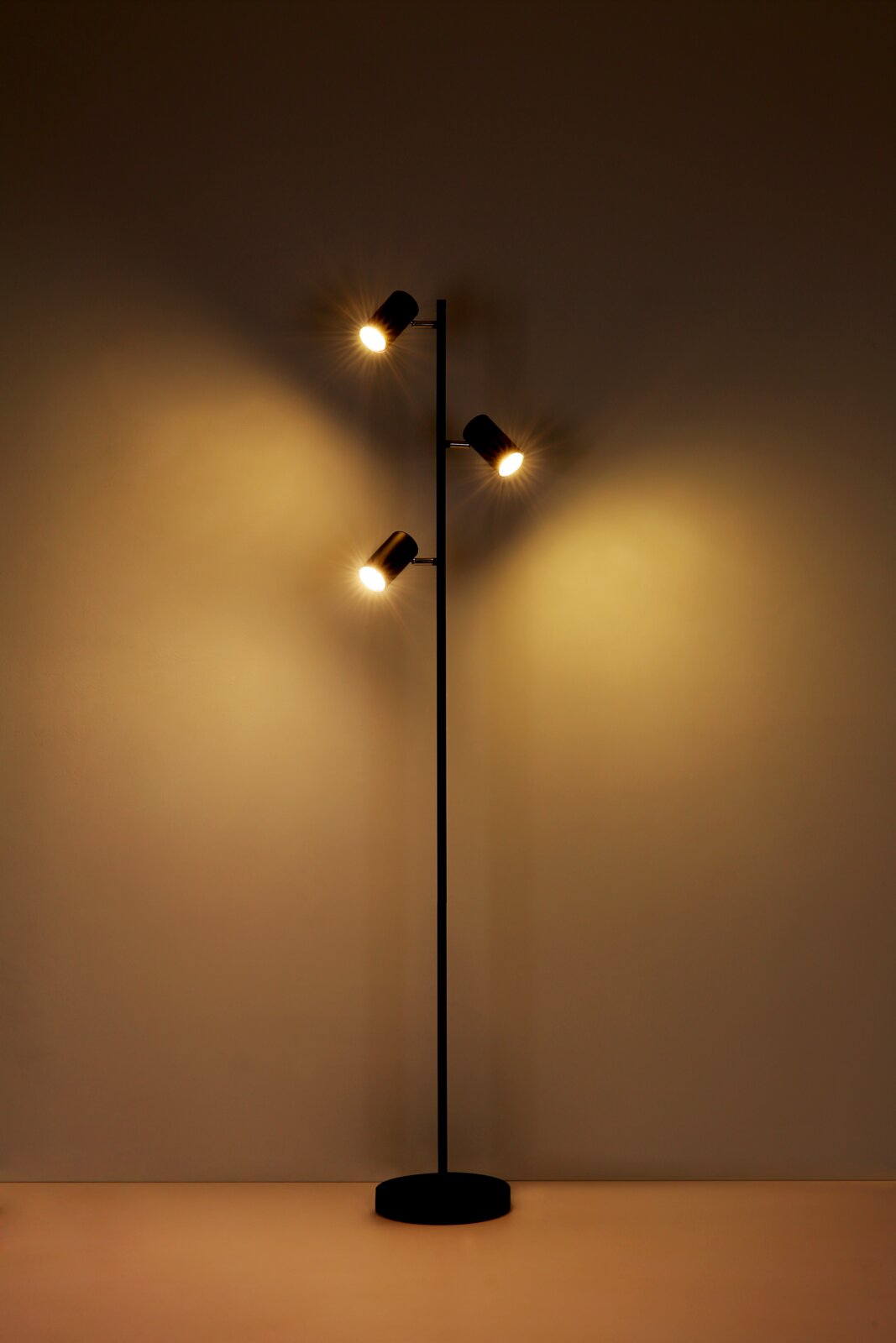 Moderne Stehleuchte mit drei verstellbaren Leuchtköpfen, die warmes Licht ausstrahlen. Ansicht von vorne.