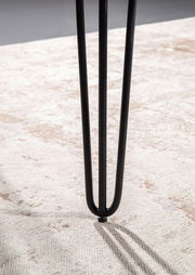 Nahaufnahme eines schwarzen Tischbeins mit Haarnadel-Design auf einem hellen Teppich.