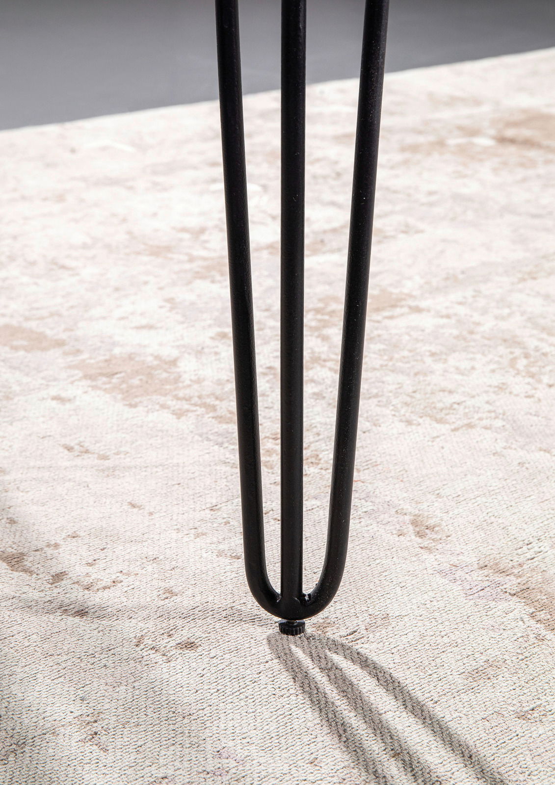 Nahaufnahme eines schwarzen Tischbeins mit Haarnadel-Design auf einem hellen Teppich.