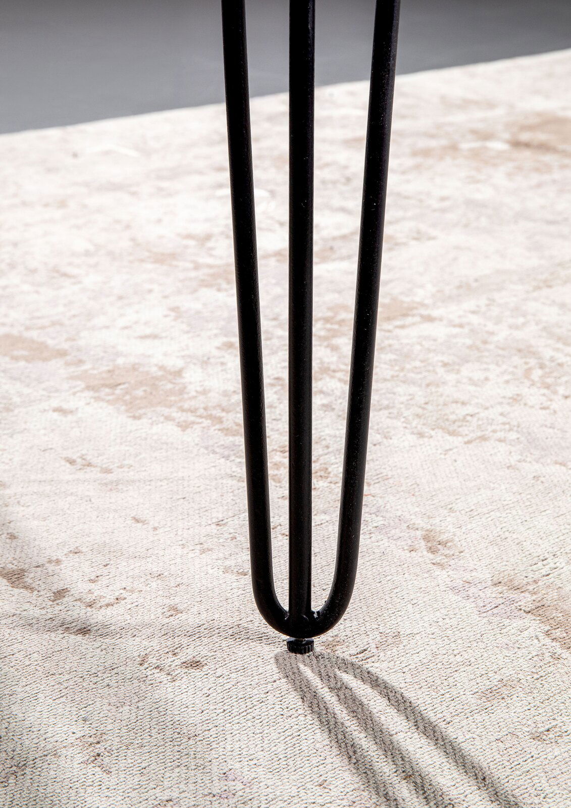 Nahaufnahme eines schwarzen Tischbeins mit Haarnadel-Design auf einem hellen Teppich.