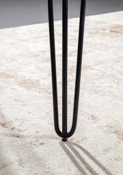 Nahaufnahme eines schwarzen Tischbeins mit Haarnadel-Design auf einem hellen Teppich.