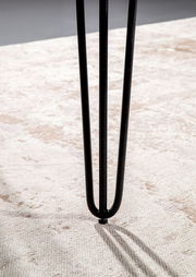 Nahaufnahme eines schwarzen Tischbeins mit Haarnadel-Design auf einem hellen Teppich.