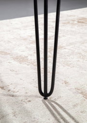 Nahaufnahme eines schwarzen Tischbeins mit Haarnadel-Design auf einem hellen Teppich.