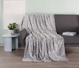 Graue Wohndecke mit Leopardenmuster, drapiert über einem dunklen Sofa, mit einem Beistelltisch und Pflanzen im Hintergrund, aus seitlicher Perspektive aufgenommen.