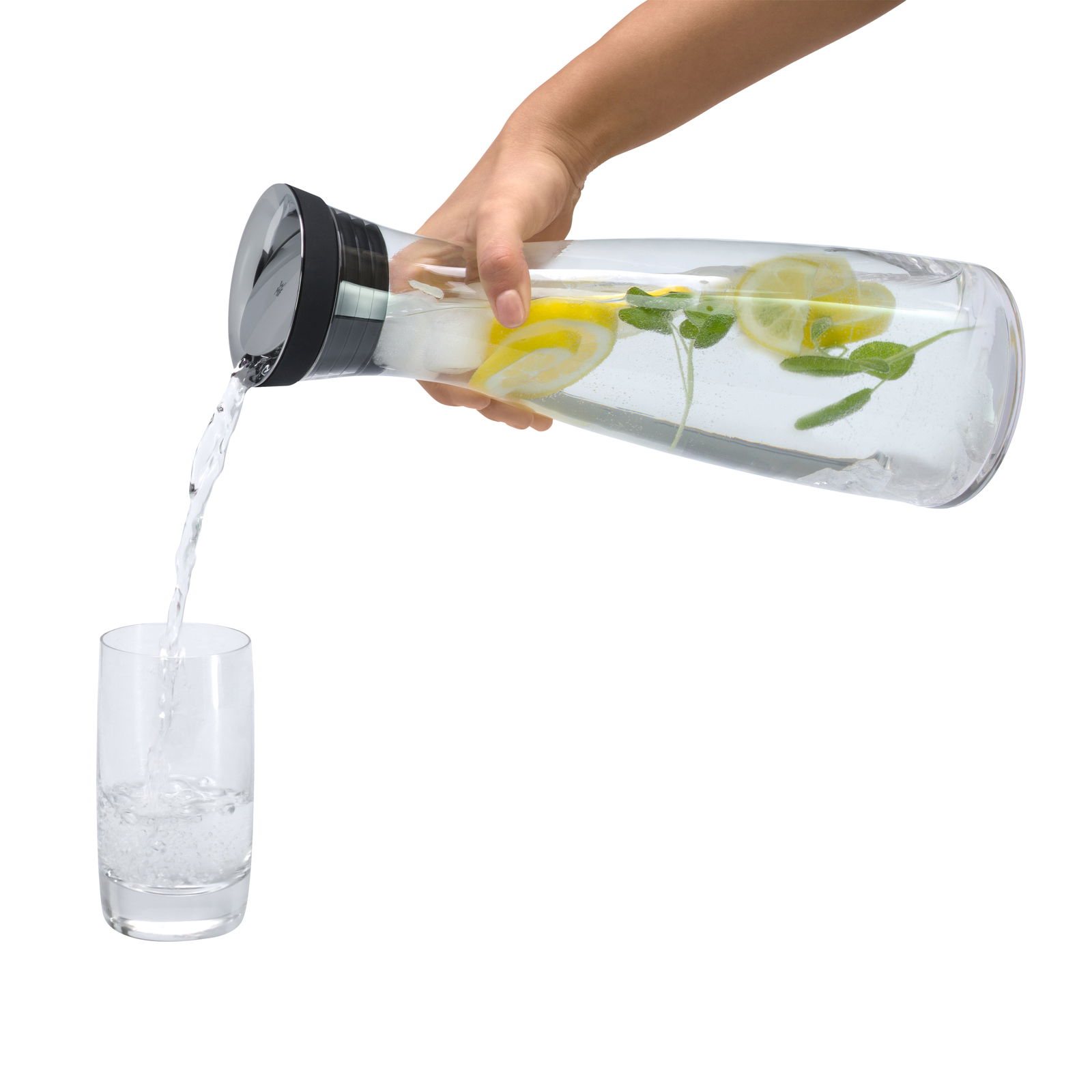 Hand gießt Wasser aus einer Wasserkaraffe BASIC 1,5L mit Zitronenscheiben und Minze in ein Glas, seitliche Perspektive