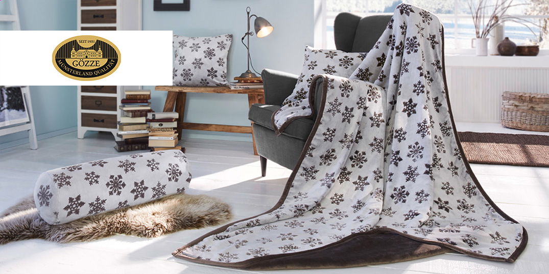 Gemütliches Wohnzimmer mit Decke, Kissen und Nackenrolle im Schneeflocken-Muster.