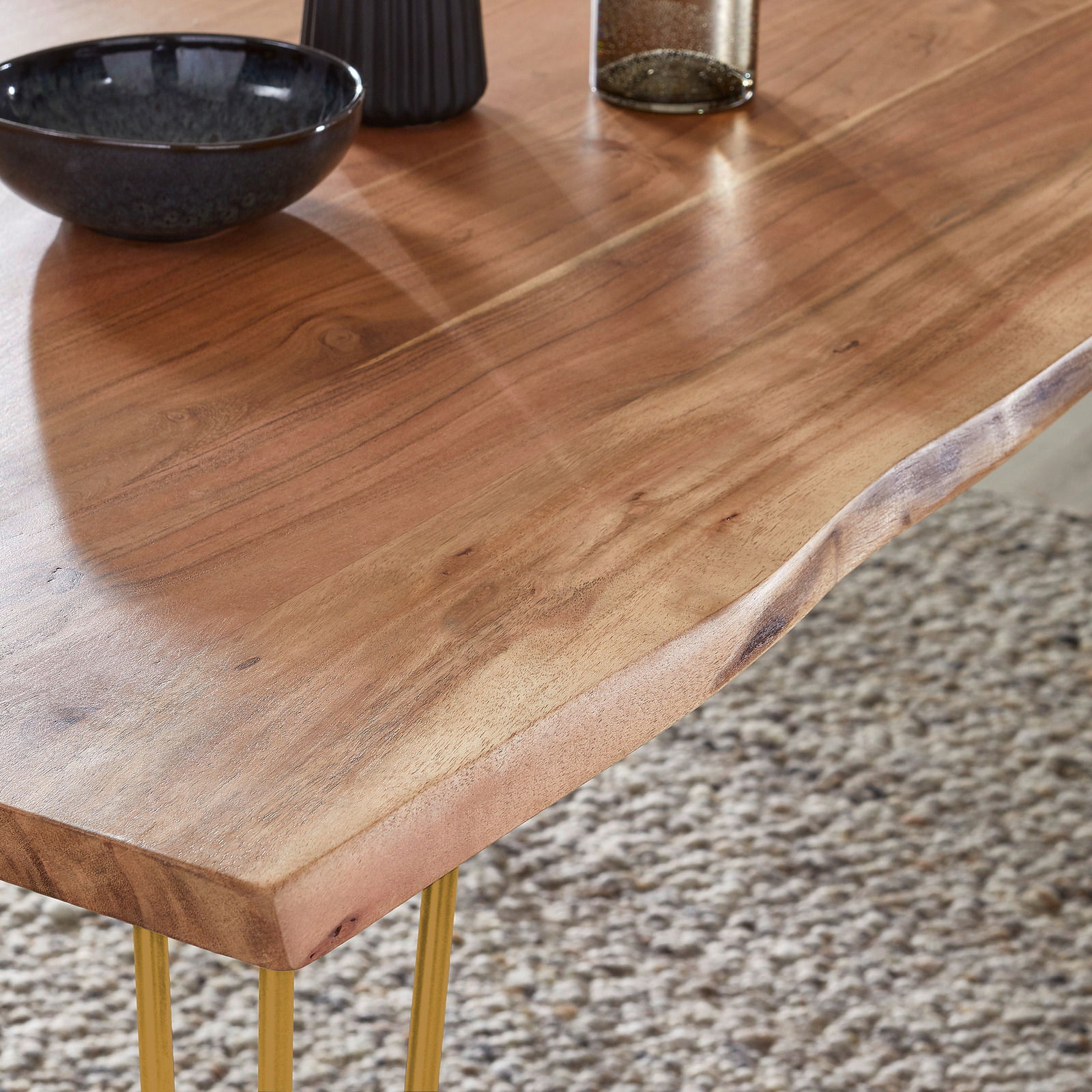 Nahaufnahme eines Esstisches aus Holz mit natürlicher Maserung und goldenen Beinen, von oben betrachtet.