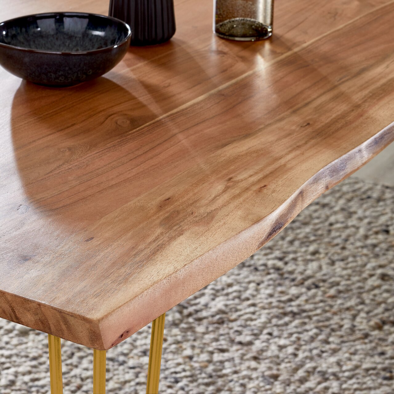 Nahaufnahme eines Esstisches aus Holz mit natürlicher Maserung und goldenen Beinen, von oben betrachtet.