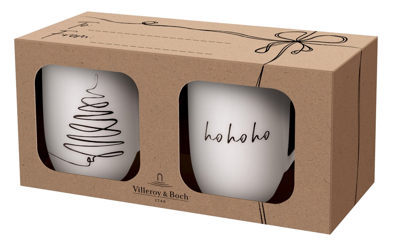 Zwei weiße Tassen in einer Geschenkbox mit Sichtfenster, eine Tasse mit einem stilisierten Weihnachtsbaum und die andere mit 'ho ho ho' Schriftzug, seitliche Perspektive.