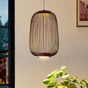 Hängelampe mit ovalem, käfigartigem Lampenschirm aus dunklem Holz/Lamellen und warmem Licht, frontal in leicht seitlicher Innenraumansicht vor heller Wand